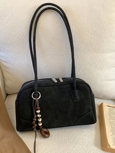 Minimalist black faux suede shoulder bag with vintage beaded charm on a beige textured sofa