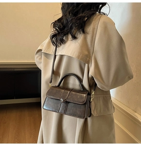 Détail du sac bandoulière vintage marron foncé avec sangle ajustable sur un manteau beige