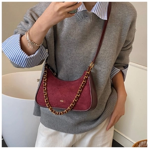 Detalle de bolso de hombro de ante granate con cadena dorada sobre un jersey gris