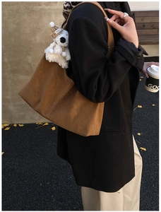 Detail of tan tote bag with white contrast stitching and a plush bear charm on strap