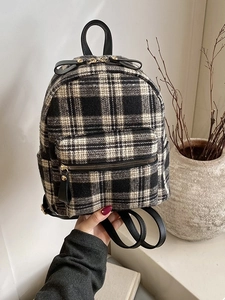 Plaid canvas backpack with black leather trim and top handle in a minimalist autumn setting