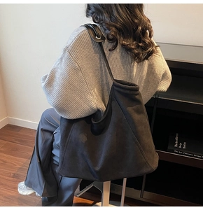 Detailed view of the large black suede tote bag shown on a shoulder in a modern room