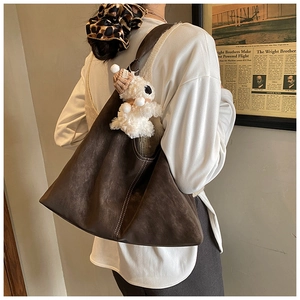 Detail view of a large brown hobo tote bag with white stitching and a cute plush charm
