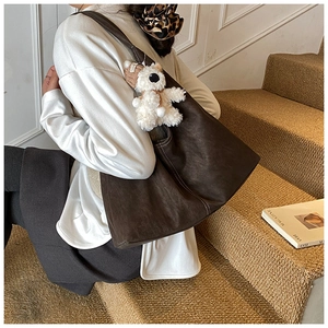 Detail of dark brown tote bag featuring white contrast stitching and plush bear charm