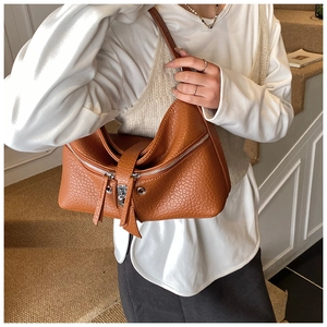 Detail of a brown lychee pattern leather tote bag with metal buckle and long zippers