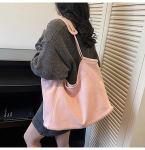 Detail view of large pink suede tote bag worn by a model for size and capacity reference