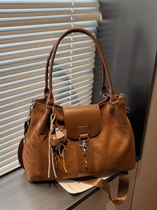 Brown vintage suede tote bag with plush bear charm and leather strap on a windowsill