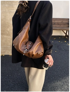 Brown pleated half-moon bag with star rivets shown in an outdoor lifestyle setting