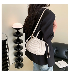 Détail du sac plissé crème avec cordons de serrage, porté par un mannequin en studio minimaliste