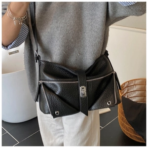 Detail of black pebbled leather crossbody bag with metal buckles and zippers on model