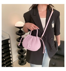 Détail d'un sac à main plissé rose avec boucle métallique et bandoulière tenu par un modèle