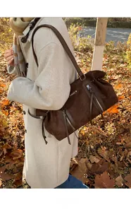 Detailed view of dark brown suede tote bag with drawstring and zip closure outdoors