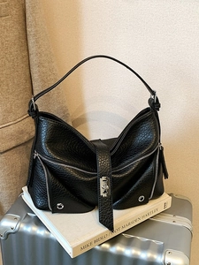 Minimalist black lychee texture leather tote bag with silver zippers on a silver suitcase