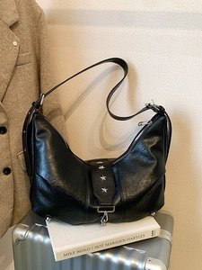 Black hobo shoulder bag with silver star rivets displayed on a silver suitcase