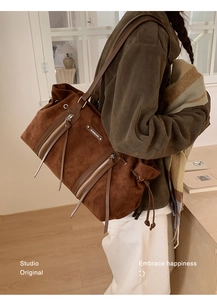 Detail of dark brown suede tote featuring long tassels and metallic logo plaque