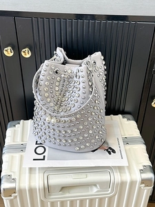 Sac seau gris clair à rivets avec chaîne argentée et détail perle posé sur une valise
