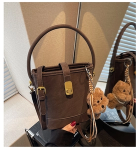 Close-up of a brown bucket bag with golden square lock and a cute plush bear charm