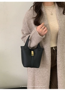Black litchi grain leather bucket bag with gold lock shown in minimalist outfit style