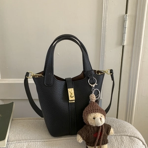 Detail of black leather bucket bag featuring gold mechanical lock and teddy bear charm