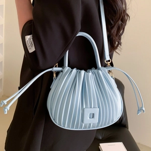 Sac nuage plissé bleu clair avec boucle carrée porté par un mannequin en blazer noir