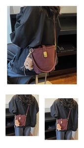 Detail view of burgundy bucket bag with gold buckle and plush bear charm accessory