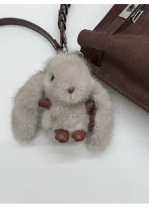 Close-up of a soft faux fur bunny keychain in light taupe attached to a brown bag