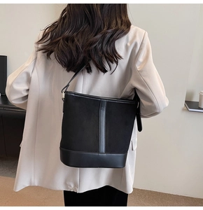 Detailed view of a black bucket bag in suede and leather mix worn by a model