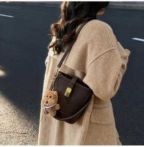 Detail of dark brown matte leather bucket bag with gold hardware and plush bear charm