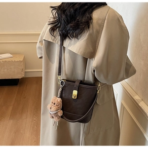 Retro dark brown bucket bag with gold lock and plush bear charm on beige trench coat