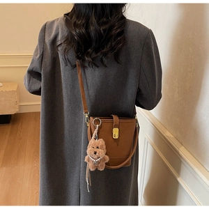Brown leather bucket bag with gold lock and plush dog charm on grey wool coat