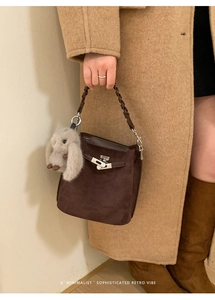 Close-up of retro dark brown suede bucket bag with silver clasp and plush bunny charm