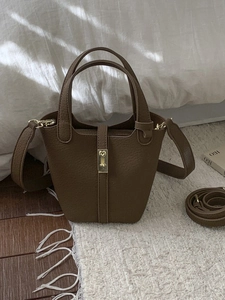 Brown litchi grain leather bucket bag with gold lock and adjustable strap in home setting