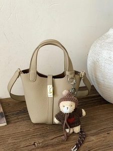 Beige lychee pattern bucket bag with teddy bear pendant on rustic wooden surface