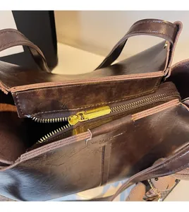 Detail of smooth gold zipper closure and oily leather texture on brown tote bag