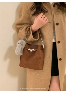 Brown suede bucket bag with woven handle and plush rabbit pendant worn by a model