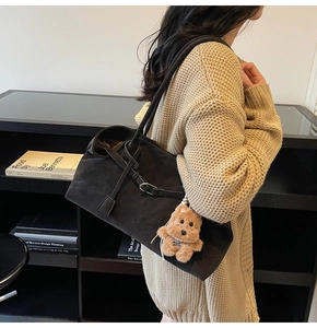 Detail of dark brown suede tote bag with plush bear charm and buckle strap decor