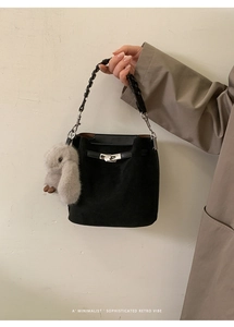Detail of black suede bucket bag featuring woven handle and plush rabbit charm