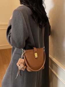 Vintage brown leather bucket bag with gold clasp and plush charm on grey winter coat