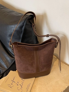 Minimalist brown suede bucket bag with adjustable leather strap and vintage aesthetic