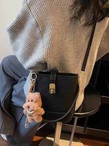 Matte black leather bucket bag with gold clasp and cute plush bear charm on a model