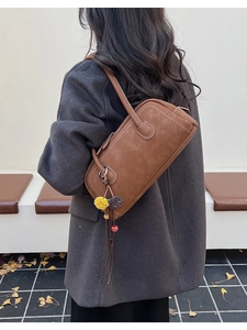 Brown rectangular shoulder bag with colorful tassels shown on model against autumn leaves