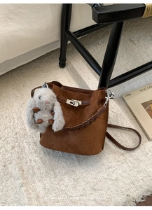 Detail of a brown suede bucket bag with a metal twist lock and woven leather handle