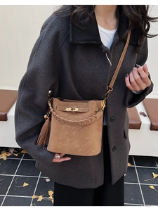 Detail of caramel bucket bag featuring woven handle and metal twist lock strap closure
