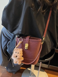 Vintage burgundy bucket bag with golden buckle and plush dog charm on a model