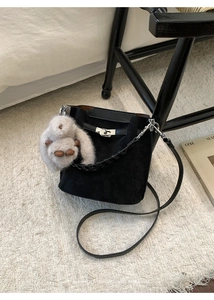 Detail of black suede bucket bag featuring woven handle and cute white bunny charm