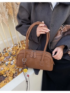 Detail view of brown retro boston bag with white stitching and fuzzy pompom charm