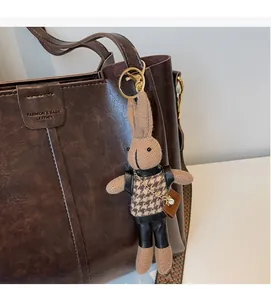 Detail of a handmade knitted rabbit keychain hanging on a brown leather tote bag