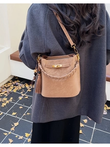 Close-up of khaki bucket bag with metal turn-lock and tassel on gray winter coat