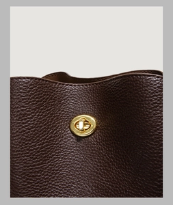 Macro shot of dark brown lychee leather texture and golden metal twist lock on bucket bag