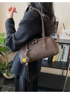 Close-up of deep coffee suede Boston bag with fringe charm and white stitching detail